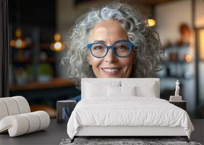 Portrait of a smiling woman with curly gray hair wearing blue-framed glasses Wall mural