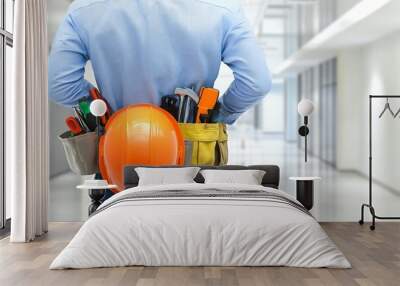 Professional worker holding safety helmet and tools in a brightly lit hallway, focus on gear Wall mural