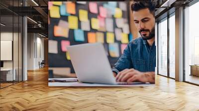 Professional working at laptop in creative workspace with vibrant sticky notes on wall Wall mural