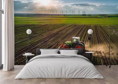 Tractor working in farmland, sun breaking through clouds, wind turbines in distance Wall mural