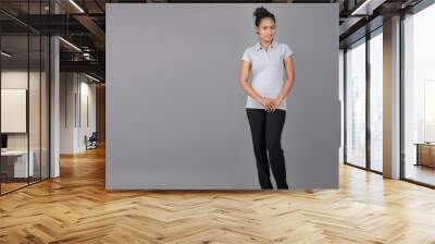 Young woman wearing grey polo t-shirt, black trousers and heels posing with cheerful expressions against grey background. Wall mural