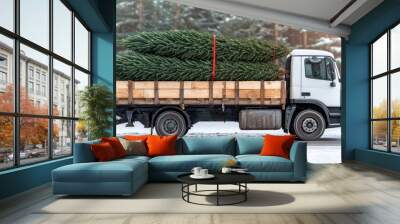 A truck carries freshly cut Christmas trees through a snowy landscape, surrounded by tall pines, evoking a festive winter scene. Wall mural