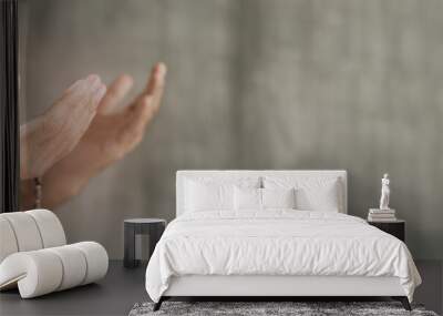 Muslim man praying with rosary beads in hand against grey wall background with copy space Wall mural