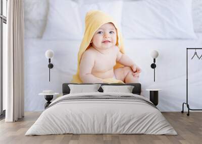 a baby girl of six months on a bed with a yellow towel on her head after bathing or washing, a small child on a cotton bed at home, the concept of care and hygiene Wall mural