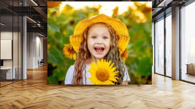 a little beautiful girl holds a sunflower in a field in summer Wall mural