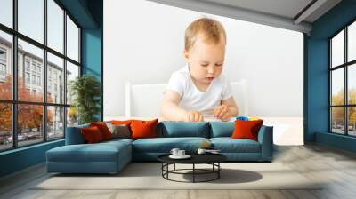 child boy 2 years old sitting at a table on a white isolated background and paints, early development, place for text Wall mural