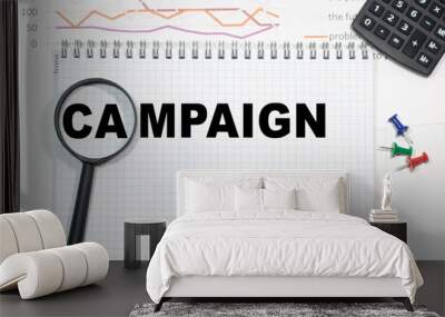 Campaign in a magnifying glass on a notepad against the background of graphs, calculator and paper clips. Wall mural