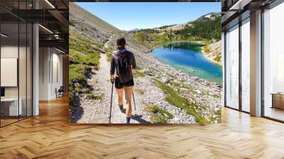 Female hiker hiking along crystal clear mountain lake. Wall mural