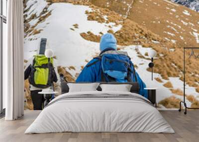 Pair of hikers descending winter traile of grass covered slope. Wall mural