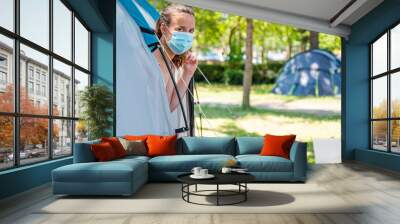 Woman wearing medical mask stepping out of camping tent. Wall mural