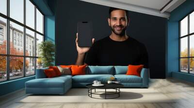 Dark-haired man in a black T-shirt holding a smartphone in front of him with a blank screen on dark gray background Wall mural