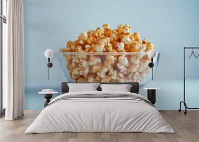 An artistic display of caramel popcorn in a glass bowl on a light blue background Wall mural