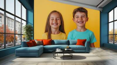 Cheerful boy and girl smiling together in front of a bright yellow background at daytime Wall mural