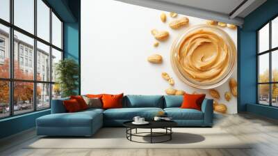 Delicious peanut butter in an open jar surrounded by scattered peanuts on a clean surface Wall mural