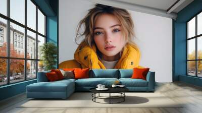 Stylish woman wearing a modern yellow puffer jacket poses elegantly against a light background Wall mural