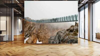 large suspension bridge connecting two mountain peaks during a foggy day in the summer Wall mural