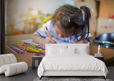 Asian girl writing  homework in book on wooden table at home Wall mural