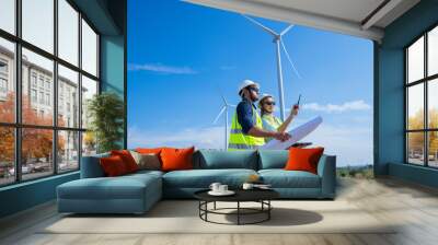 Engineer wearing uniform ,helmet hold document inspection work in wind turbine farms rotation to generate electricity energy. Green ecological power energy generation wind sustainable energy concept. Wall mural