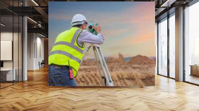 Surveyor engineer wearing safety uniform and helmet with equipment theodolite to measurement positioning on the construction site of the road with construct machinery background Wall mural