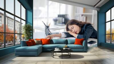 A woman is sleeping on her desk with a laptop and a stack of papers Wall mural