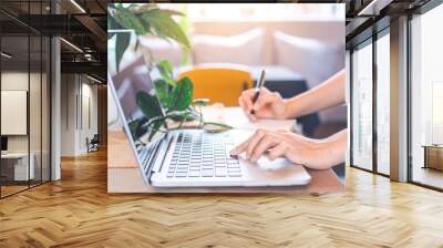 Woman hand works in a laptop computer and writing on notepad with a pen in the office. Wall mural