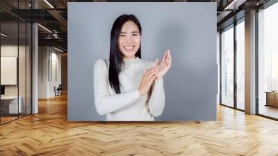 Smiling asian woman wears cream sweater standing on gray background Wall mural