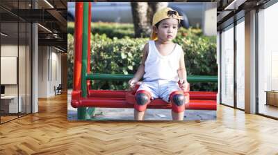 Asian kid 2 year old from Thailand sitting on the garden alone. He using a safety cycling protection equipment concept. and he looking the wood on his hands.                               Wall mural