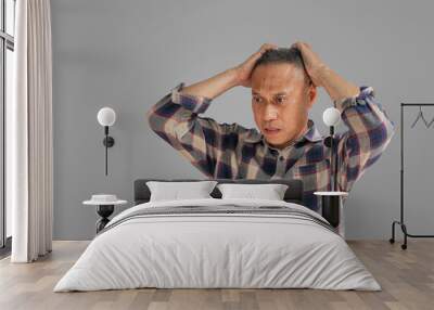 A middle-aged man wearing a plaid shirt uses his hand to touch his head because he has a headache due to a migraine or stress while standing on a gray background. stress concept. Clipping Path Wall mural