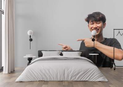 A young Asian man in his 20s wearing a black t-shirt making a welcome gesture or presenting isolated on a gray background. Space for advertisements or welcome messages. Happy man Wall mural