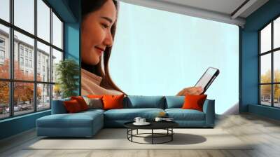 Asian young woman online with mobile in living room near the window Wall mural