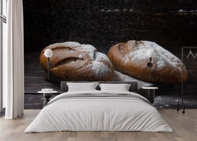 Two black bread with flour on a wooden background. Advertising bread. Leaning flour. Wall mural