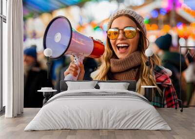 Joyful young woman in trendy autumn fashion smiling and making an announcement with a megaphone at a festive outdoor event. Wall mural