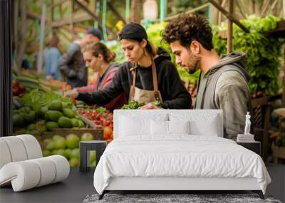 Young man selecting fresh tomatoes at a vibrant local farmers market, surrounded by a variety of organic produce. Wall mural