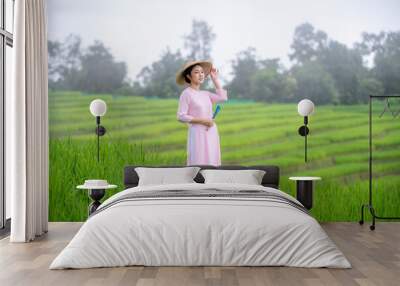 Beautiful women standing in a lush green tea field, likely in a rural area. They are wearing traditional conical hats and light-colored clothing with green tea platation background	 Wall mural