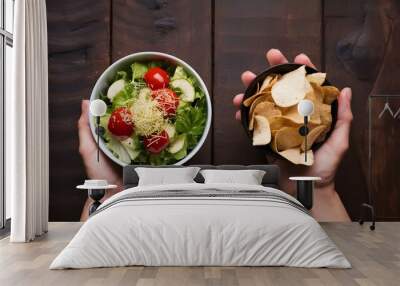 One hand holding bowl of vegetable salad, other holding chips. Healthy natural organic fresh vegetarian food vs unhealthy processed fast junk food. Lunch or snack decision Wall mural