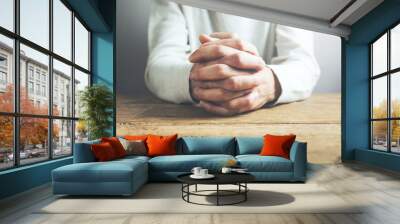 Hands of praying young man on a wooden desk background. Wall mural