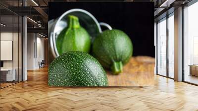 Close-up of a round zucchini lying on burlap cloth, two more zucchini in the background in a metal bucket, with selective focus, on rustic table and black background, in vertical Wall mural