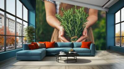 A woman is holding a bunch of fresh herbs, including rosemary, in her hands Wall mural