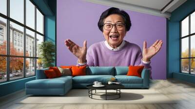 Excited elderly Asian woman with glasses wearing sweater on plain lavender background Wall mural