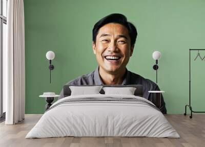 Joyful middleaged Asian man with short black hair wearing casual shirt on plain green background Wall mural