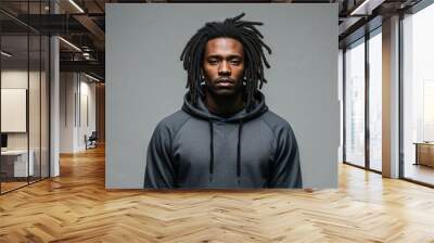 Serious young Black man with dreadlocks wearing hoodie on plain grey background Wall mural