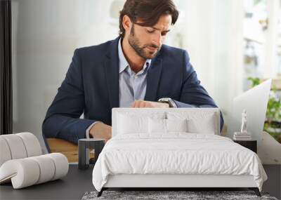 Keeping an eye on the time. A handsome businessman checking the time on his watch at his desk. Wall mural