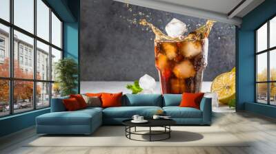  cola drink in glass with ice cubes creating a splash and bubbles on gray background with sliced lemon and mint leaves Wall mural