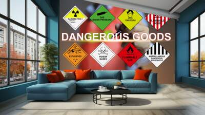 A warehouse worker in a reflective coat points with a pen at the words Dangerous goods letters and the symbols of the various types of dangerous goods involved. Wall mural