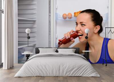 Girl eats sausage near the refrigerator Wall mural