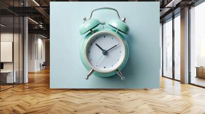 vintage alarm clock in soothing mint green color stands against soft blue background, evoking sense of calm and nostalgia. Its classic design features round face with clear markings and two bells on Wall mural