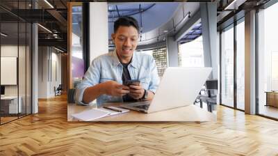 Asian man happy and smile face with blue shirt using laptop and mobile phone in coffee shop, online freelance business Wall mural