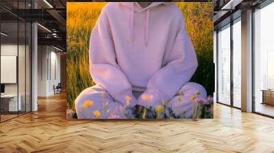 Hoodie Mockup - A person in a soft pink hoodie sits peacefully in a field of flowers during sunset. Wall mural