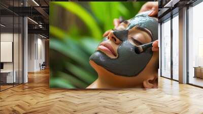 Woman receiving facial treatment with a black mud mask Wall mural