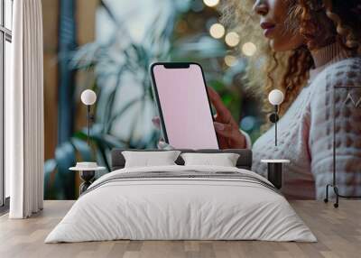 Woman with curly hair holding a smartphone with a pink screen Wall mural